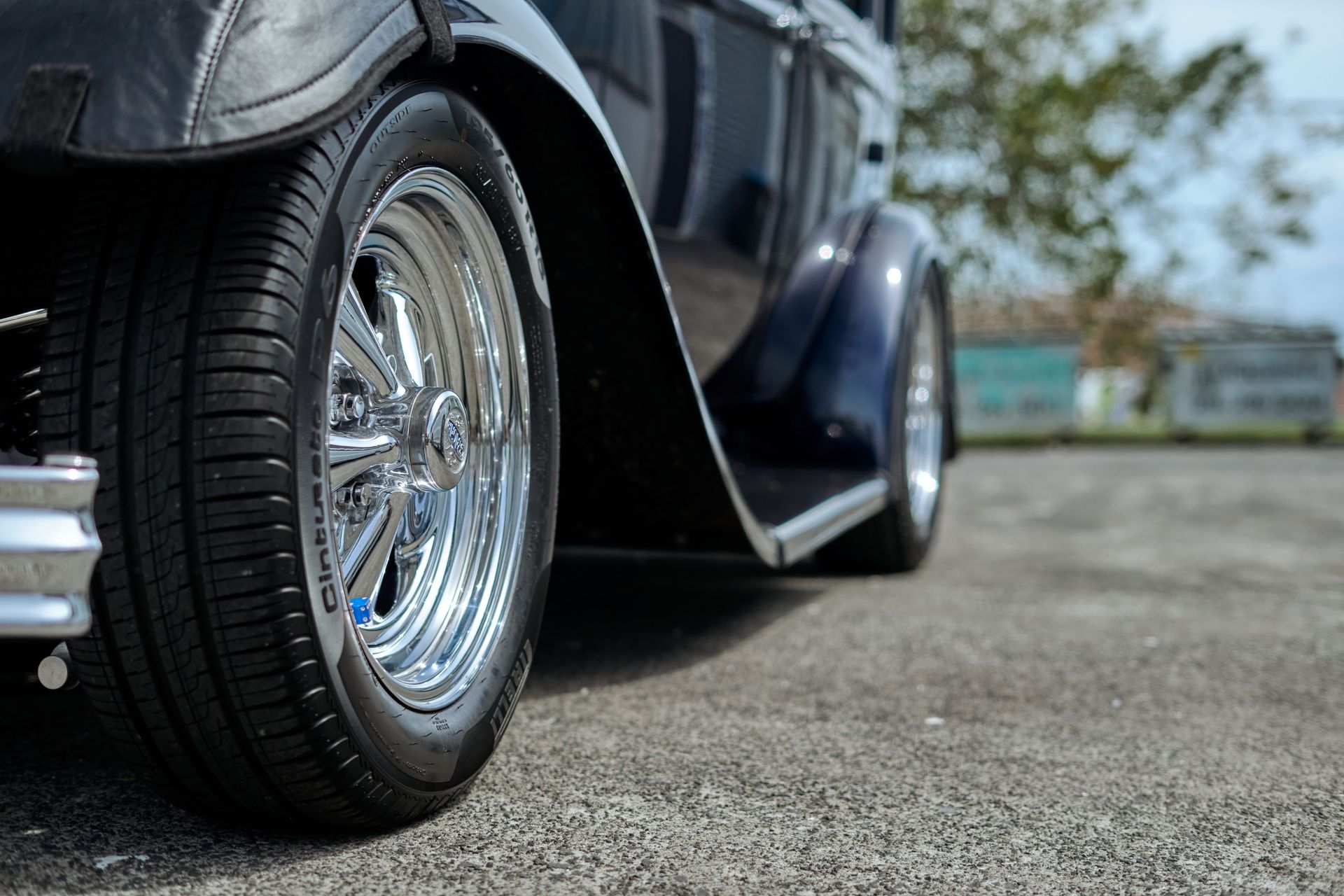 Detailed view of a chrome wheel on a vintage hot rod in an outdoor setting in Auckland.